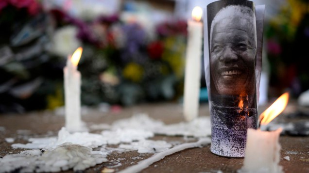 Vela queima ao lado da foto de Nelson Mandela. Multidão faz vigília do lado de fora do hospital, e presta homenagens com flores e cartazes