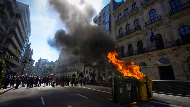 Trabalhadores dos estaleiros ficam perto de um latão de lixo pegando fogo durante uma manifestação contra o pagamento de auxílios estatais pelos estaleiros espanhóis em Vigo nesta quinta-feira (04), na Espanha