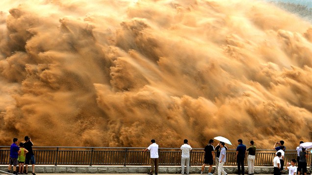 Visitantes assistem a água jorrando no Reservatório Xiaolangdi sobre o Rio Amarelo, durante uma operação de lavagem de areia em Jiyuan, província de Henan, na China