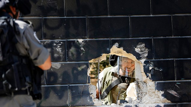 Um policial de fronteira de Israel olha para o seu colega através de um buraco em uma seção da barreira controversa israelense na Cisjordânia, na aldeia de Abu Dis, perto de Jerusalém, na terça-feira (09)