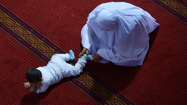Muçulmana segura uma criança durante as orações na primeira noite do mês sagrado do Ramadã na mesquita Istiqlal, em Jacarta, Indonésia, na terça-feira (09)