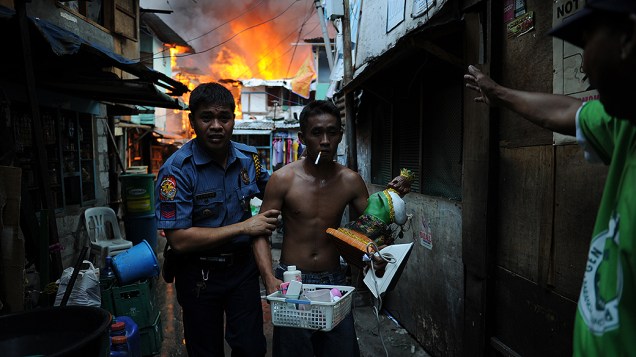 Policial retira um morador de sua casa em chamas durante incêndio em uma favela no distrito financeiro de Manila, na quinta-feira (11)