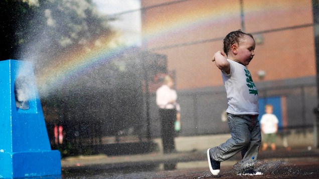 Menino se refresca do calor em um aspersor de um parque infantil no bairro de Brooklyn, em Nova York, nesta segunda-feira (15)