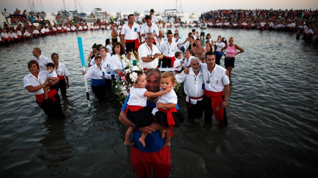 Homem segura seus filhos vestidos com trajes tradicionais enquanto a estátua da Virgem El Carmen é levada para o mar nesta quarta-feira (17), durante uma procissão em Málaga, na Espanha