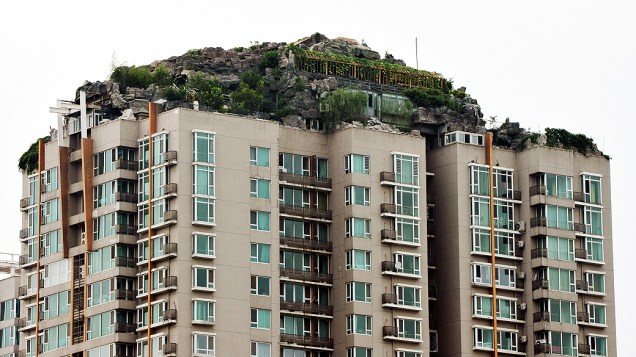 Um excêntrico morador local construiu uma casa em meio ao que parece uma pilha de rochas e árvores no topo de um prédio de 26 andares na capital chinesa. Vizinhos reclamam com medo de que a mansão, com mais de 1.000 m², provoque um desmoronamento