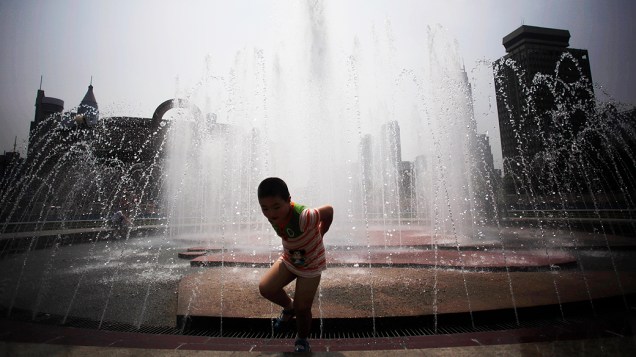 Menino se refresca nesta quinta-feira (29) em fonte de parque de Xangai, na China