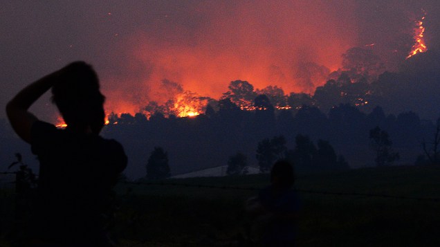 Mais de cem incêndios sem controle foram registrados nos Estados australianos de Nova Gales do Sul e Victoria. Na foto mulher observa chamas que se aproxima de uma área residencial do oeste de Sidney, nesta terça-feira (10)