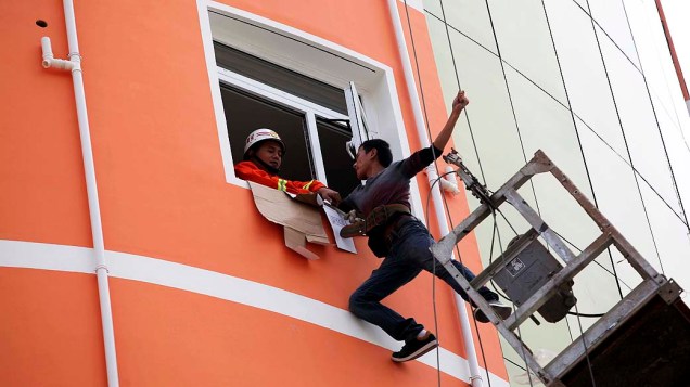Em imagem divulgada nesta terça-feira (10), bombeiro tenta resgatar trabalhador que ficou preso em plataforma suspensa a 18 metros de altura no exterior de prédio de LiuAn, província de Anhui (China)