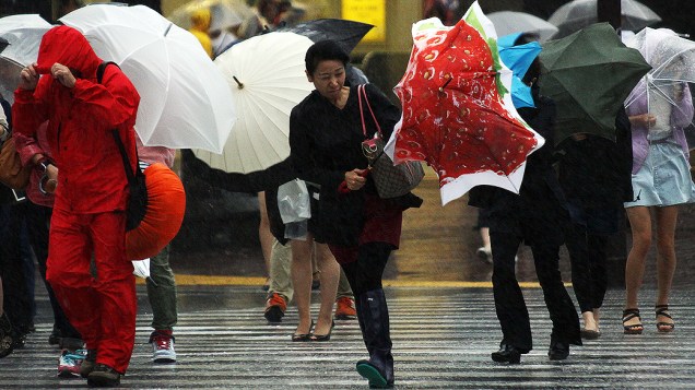 Pedestres caminham contra o vento forte e chuva em Tóquio nesta segunda-feira (16)