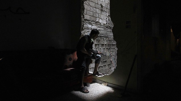 Um membro da brigada Shohadaa Badr, que opera sob o Exército Livre da Síria, olha através de um buraco na parede em Ashrafieh, Aleppo 