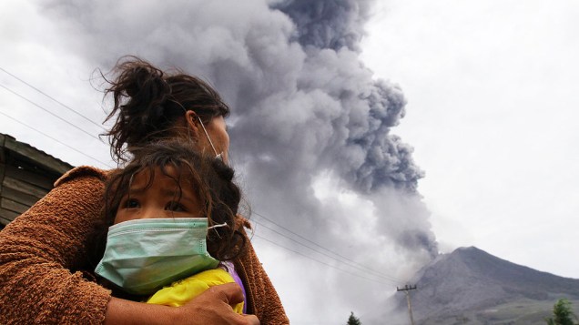 Mãe segura filha durante uma erupção do Monte Sinabung em Perteguhan, na Indonésia. Autoridades preparam abrigos temporários para os desabrigados