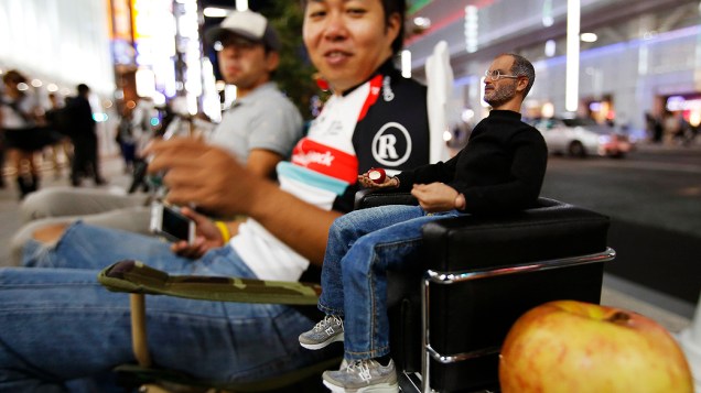 Pessoas se sentam ao lado de uma estatueta do co-fundador da Apple Steve Jobs enquanto esperam para o lançamento do novo iPhone 5S da Apple, no distrito comercial em Tóquio