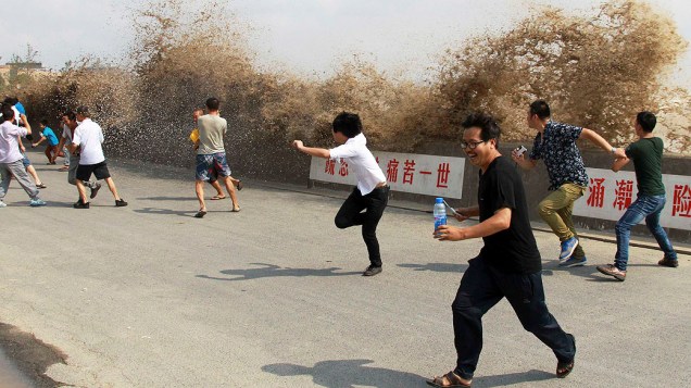 Turistas fogem de uma pororoca que atingiu uma barreira às margens do rio Qiantang em Hangzhou, província de Zhejiang, na China