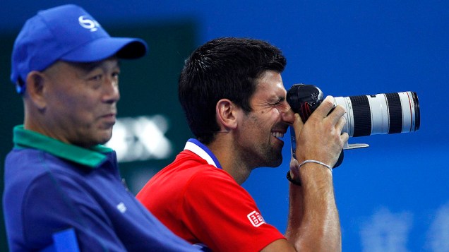 Novak Djokovic tira fotos com uma câmera durante uma partida beneficente com a chinesa Li Na para marcar a abertura do China Open Tennis Tournament, em Pequim