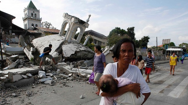 Mulher carrega um bebê em frente a uma igreja destruída em Tubigon, Bohol, um dia depois que um terremoto atingiu a região central Filipinas Mulher carrega um bebê em frente a uma igreja destruída em Tubigon, Bohol, um dia depois que um terremoto atingiu a região central Filipinas