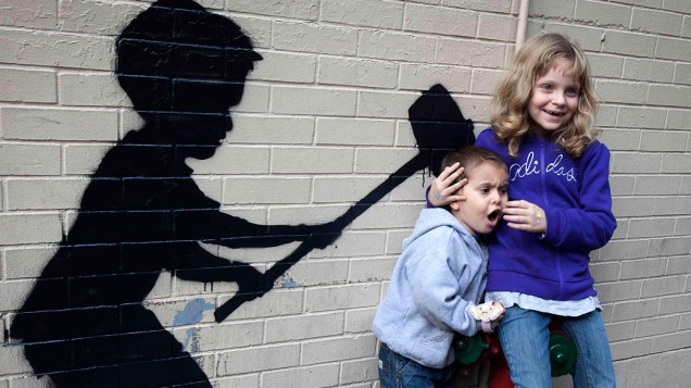 Crianças posam para uma foto em frente a um grafite do artista Banksy, em Nova York
