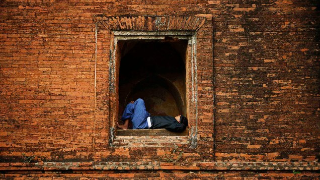 Um homem é visto dormindo em uma janela do famoso templo budista Dhammayangyi, na cidade de Bagan na Birmânia