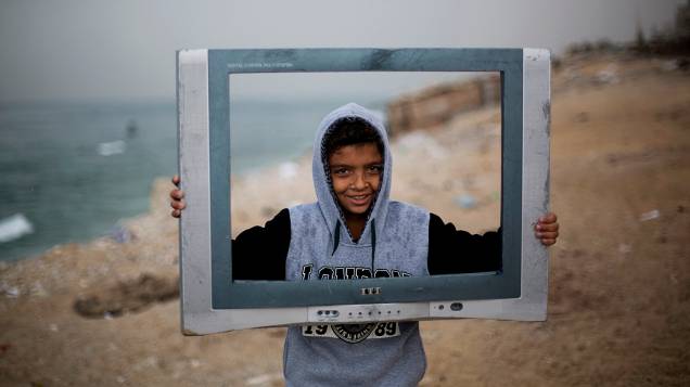 Menino palestino brinca com uma TV quebrada do lado de fora de sua casa no campo de refugiados em al-Shatee na cidade de Gaza
