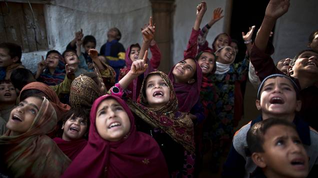 Crianças refugiadas afegãs e paquistanesas cantam antes do início da aula improvisada na periferia de Islamabad, no Paquistão