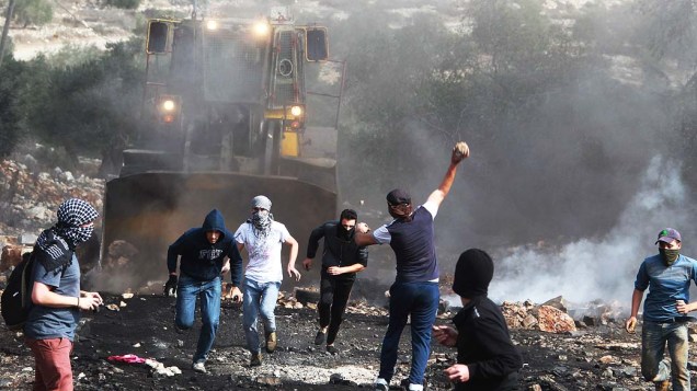 Manifestantes atiram pedras em um trator do exército israelense durante protesto contra a desapropriação de terras palestinas por Israel na aldeia de Kfar Qaddum, no norte da Cisjordânia