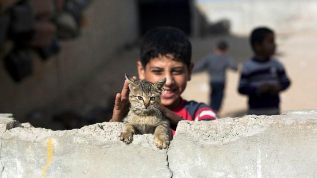 Menino brinca com seu gato em uma casa abandonada, na Faixa de Gaza Menino brinca com seu gato em uma casa abandonada, na Faixa de Gaza