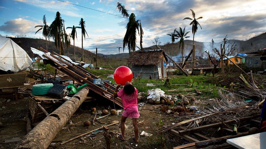 Menina brinca com uma bola nos escombros onde a casa de sua família foi arrasada por um coqueiro durante o tufão Haiyan, nos arredores de Tacloban, nas Filipinas