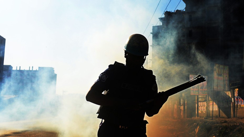 Policial da tropa de choque de Bangladesh recarrega arma em confronto com manifestantes, nesta terça-feira (19)