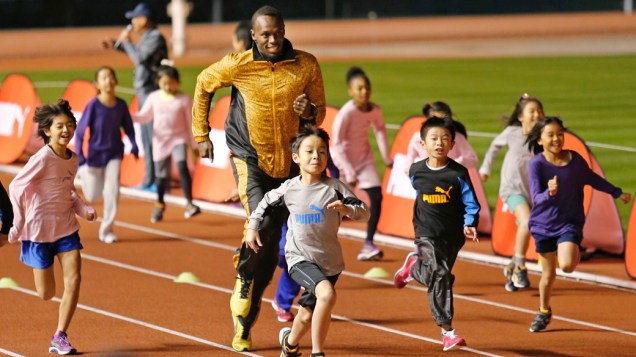 Usain Bolt corre com crianças no Estádio Nacional, em Tóquio, no Japão