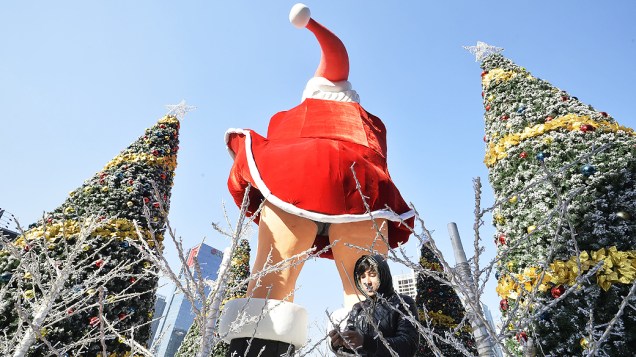 Homem decora árvores de Natal ao lado de um boneco do Papai Noel que reproduz uma cena de Marilyn Monroe em um shopping em Taiyuan, China
