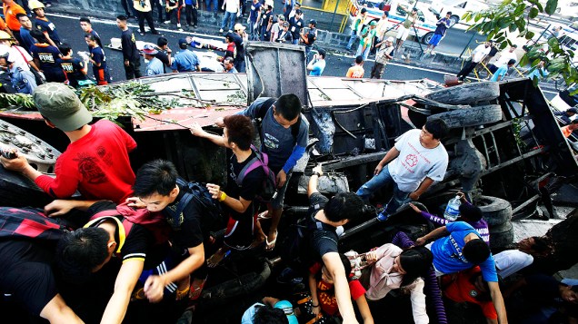 Pedestres caminham por cima de ônibus acidentado enquanto tentam atravessar rua bloqueada pelo veículo, em Manila, nas Filipinas. Pelo menos 21 pessoas morreram depois que o ônibus capotou ao cair de uma via expressa elevada e bater contra uma van