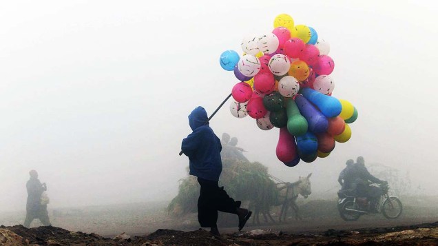 Vendedor de balões paquistanês anda em meio à neblina em manhã fria