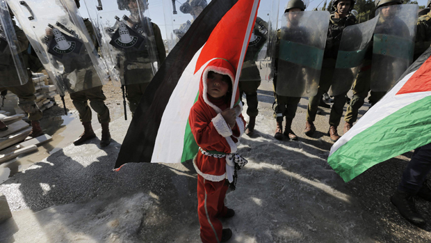 Menino palestino vestido como Papai Noel na frente de uma barricada de soldados israelenses durante um protesto perto de Belém