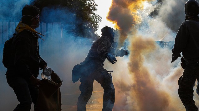 Manifestante de oposição ao governo atira uma bomba de gás lacrimogêneo em direção aos policiais durante confrontos no centro de Bangcoc, na Tailândia