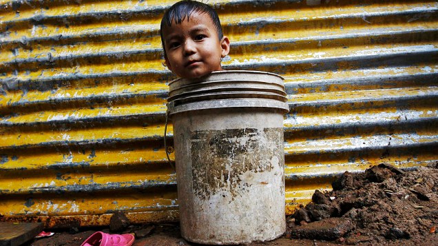 Um menino dentro de um balde enquanto esperava por sua mãe para tomar banho em uma cabana improvisada na cidade indiana de Chennai 