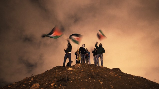 Manifestantes erguem bandeiras enquanto aguardam a libertação de prisioneiros em Jerusalém. Israel libertou 26 prisioneiros palestinos em negociações de paz mediadas pelo secretário de Estado dos Estados Unidos John Kerry, em Israel Manifestantes erguem bandeiras enquanto aguardam a libertação de prisioneiros em Jerusalém. Israel libertou 26 prisioneiros palestinos em negociações de paz mediadas pelo secretário de Estado dos Estados Unidos John Kerry, em Israel
