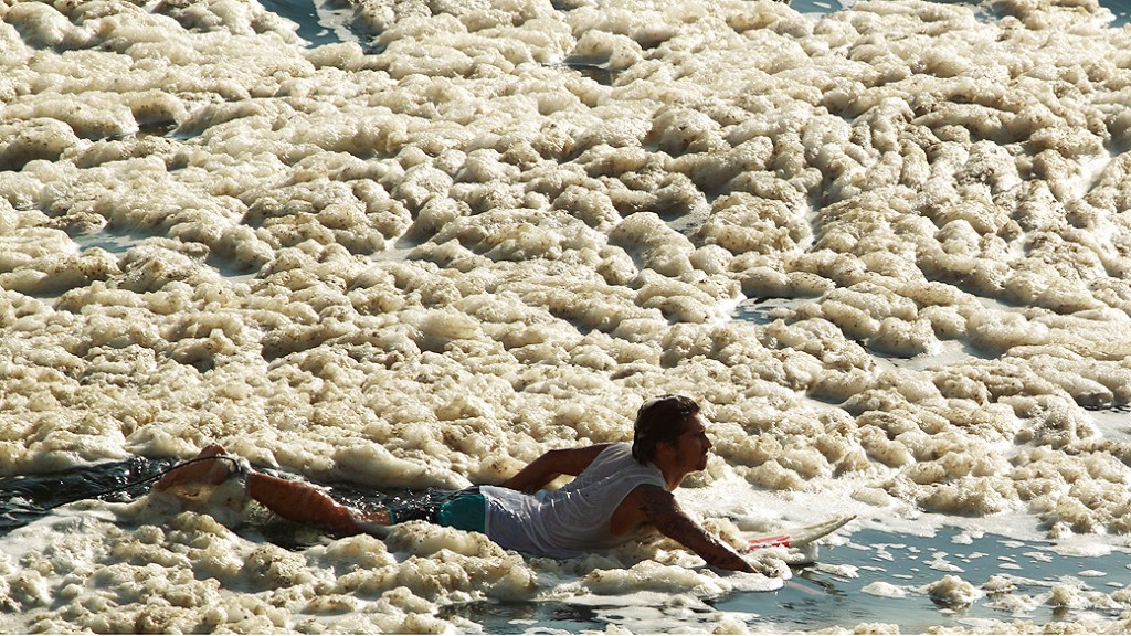 Surfistas pegam onda no Leblon ao meio à espuma, na segunda-feira: poluição das praias é uma das consequências do baixo investimetno em saneamento