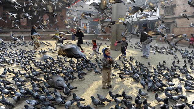 Crianças alimentam pombos na Praça Durbar em Katmandu, no Nepal. O local está na lista de patrimônios mundiais da Unesco