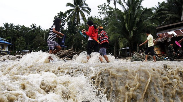 Pessoas atravessam ponte danificada após deslizamento de terra em Lupon, nas Filipinas, nesta segunda (13). Pelo menos nove pessoas morreram e quatro estão desaparecidas