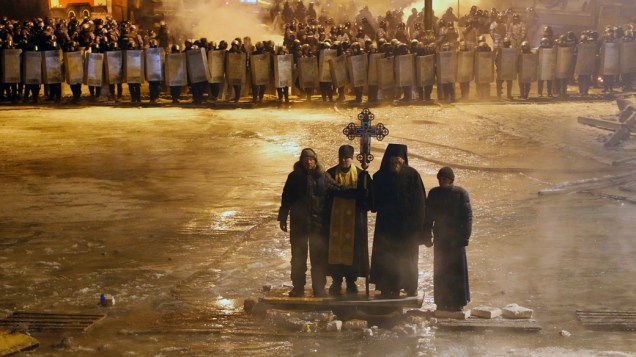 Padres ortodoxos rezam entre os ativistas pró-europeus e linhas de policiais no centro de Kiev, na Ucrânia