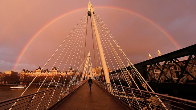 Arco-íris aparece enquanto um pedestre atravessa a Ponte Hungerford em Londres 