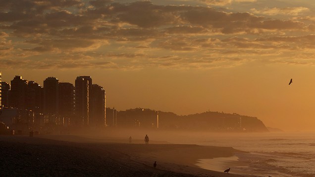 Homem caminha na praia da Barra da Tijuca praia durante o nascer do sol no Rio de Janeiro nesta sexta-feira (31)