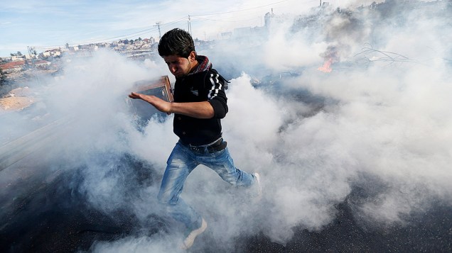 Manifestante palestino atravessa uma nuvem gás lacrimogêneo disparado por soldados israelenses durante confrontos em Jalazoun no campo de refugiados perto da cidade de Ramallah, na Cisjordânia