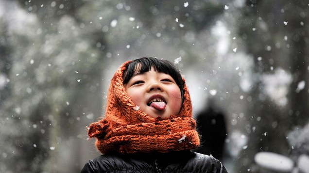 Menina poe a língua para fora para comer flocos de gelo durante nevasca em uma rua em Hefei, província de Anhui, na China 