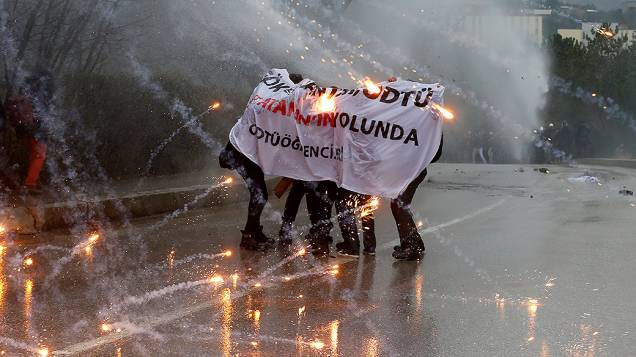 Manifestantes se protegem de jatos de água da polícia e de fogos de artifício, lançados por outros manifestantes, durante uma protesto contra a abertura de uma nova estrada, em Ancara, na Turquia