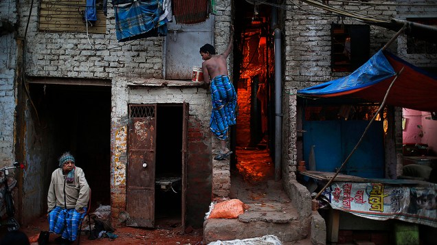 Homem prende um balde com a boca enquanto desce de um quarto de cortiço, em uma favela em Nova Délhi, na Índia