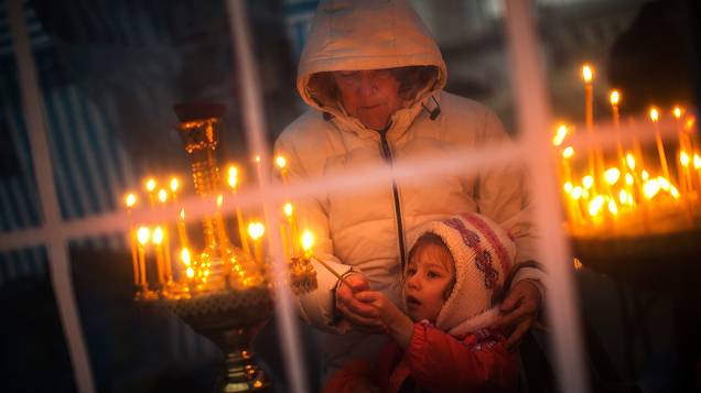 Mulher ajuda seu filho a acender uma vela dentro de uma igreja improvisada na Praça da Independência, o epicentro das manifestações em Kiev, na Ucrânia