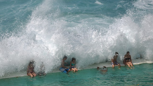 Ondas quebram sobre pessoas sentadas na borda de uma piscina de água salgada na praia de Bondi, em Sydney, nesta sexta-feira de Páscoa (18). Australianos aproveitam o feriado da Semana Santa até terça-feira (22)