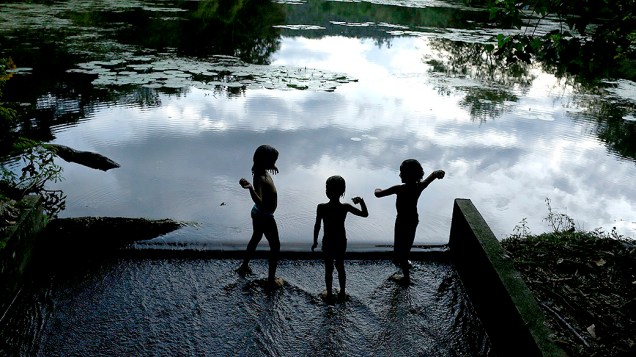 Crianças brincam na margem de uma lagoa na Reserva Ecológica de Guapiaçu, no Rio
