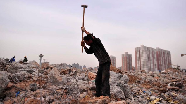 Homem recicla barras de metal em demolição, na China