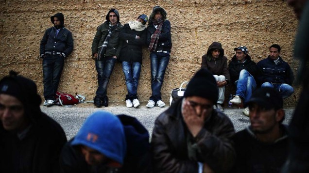 Imigrantes esperam ônibus para  alojamento temporário no porto de Lampedusa, Itália. Com os protestos no Egito e Tunísia, aumentaram o número de imigrantes na União Européia